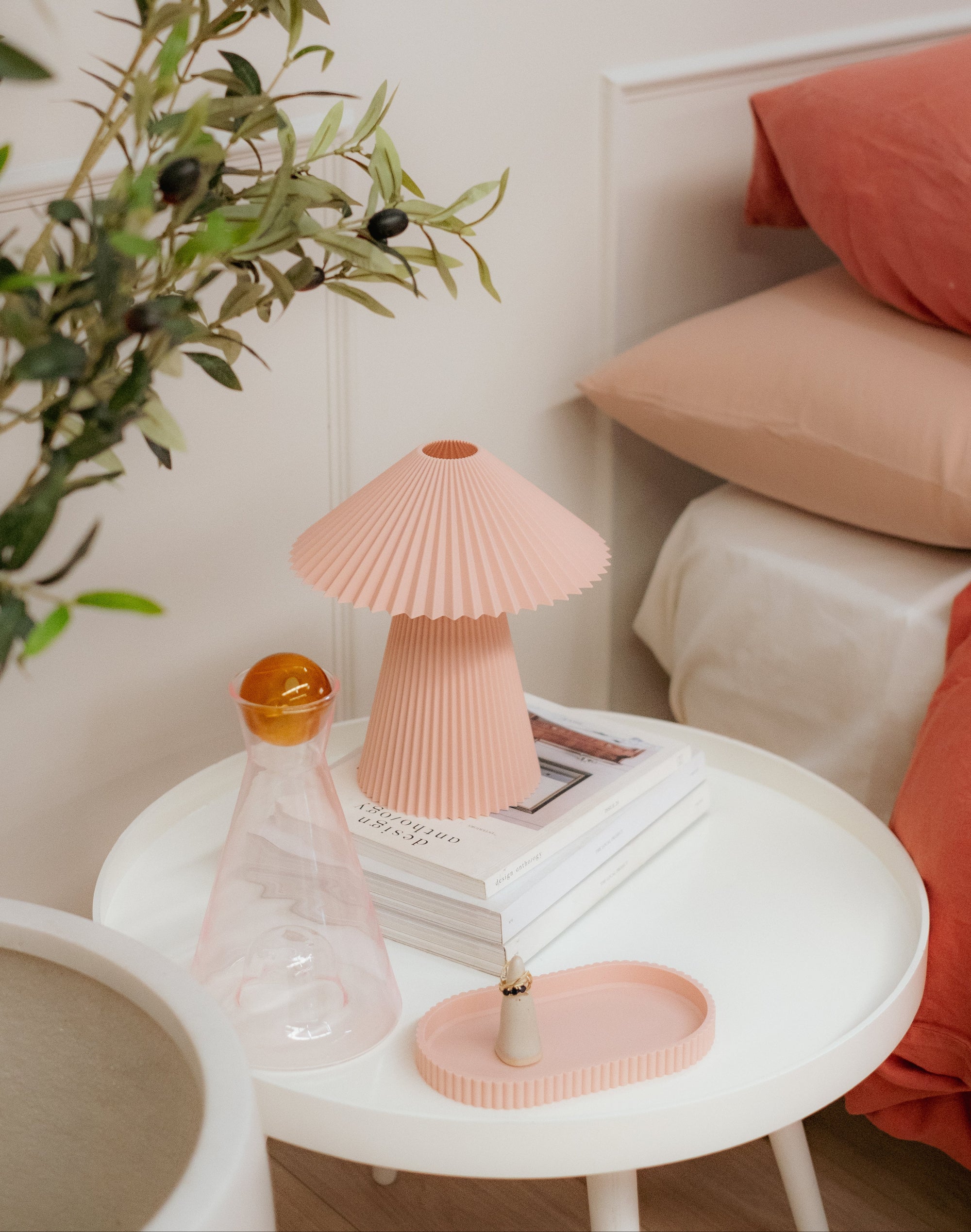 Small round table with a pink lamp and decorative items against a light-colored wall.